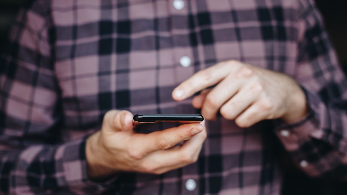 A close up on a man holding a phone and using it with one of his fingers
